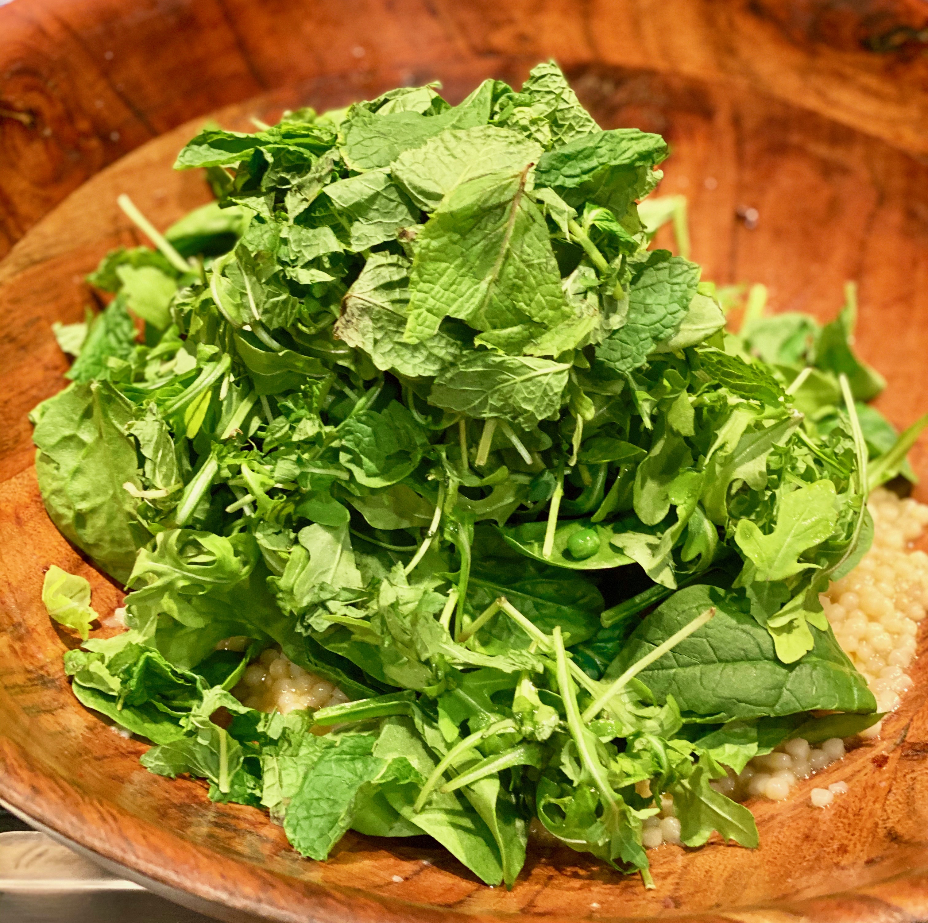 a generous pile of mint, arugula and spinach in a large wooden salad bowl 