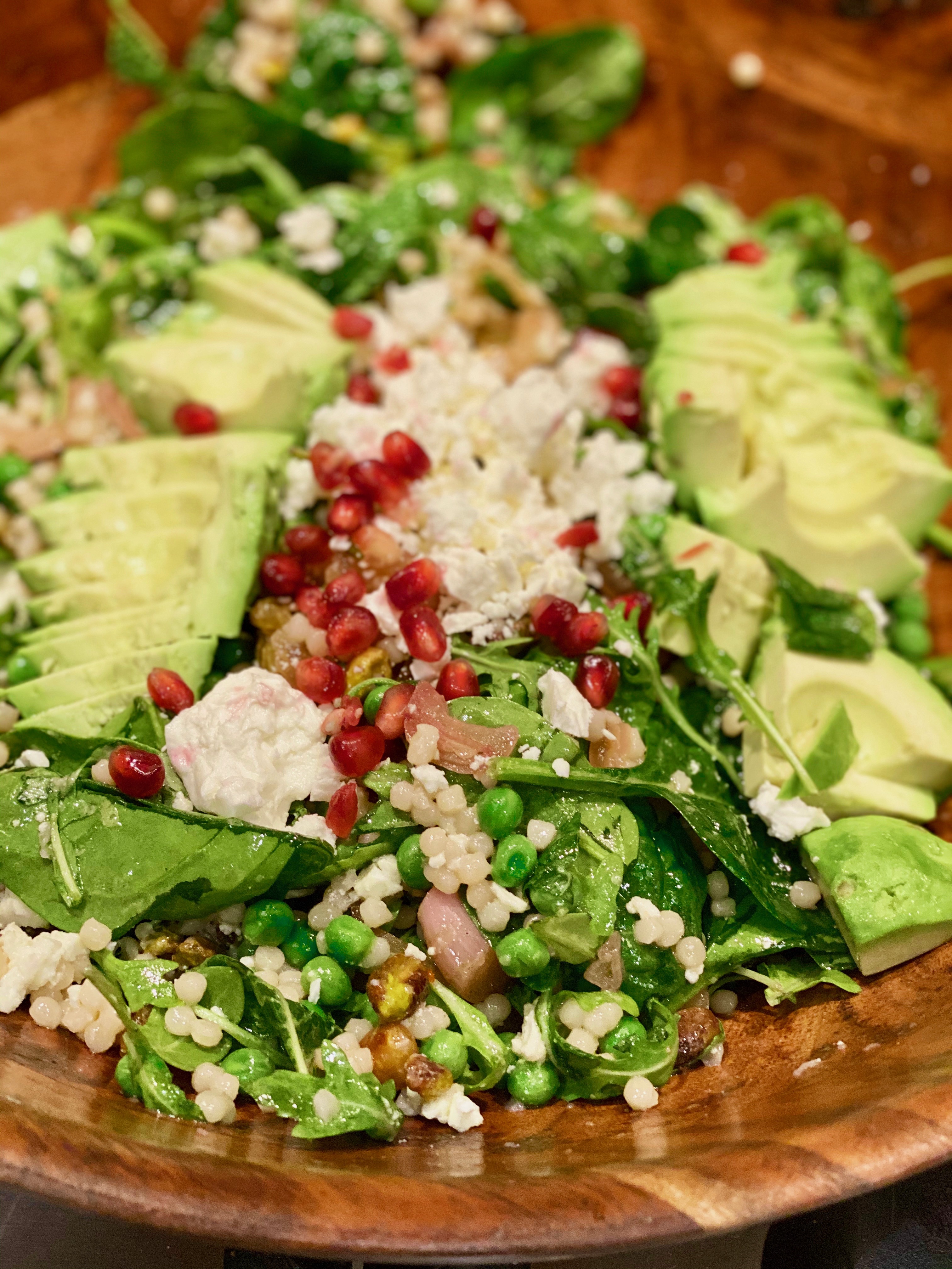a close up picture of feta cheese, pomegranate arils, avocado and greens in a large salad bowl 