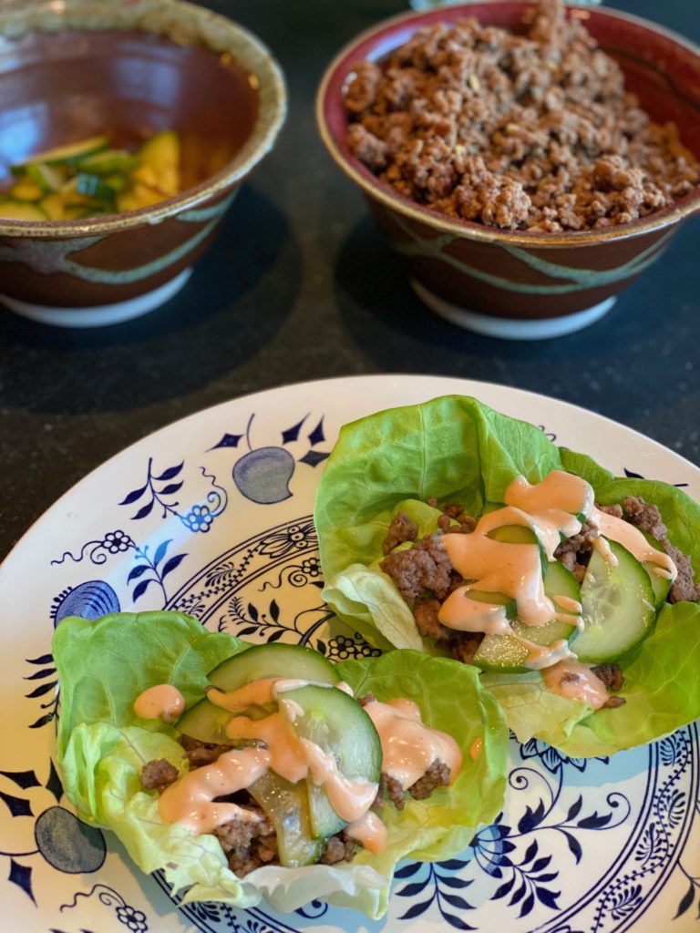 a blue and white plate with lettuce leaves, ground beef and cucumbers drizzled with a bit of thick pale orange sauce 