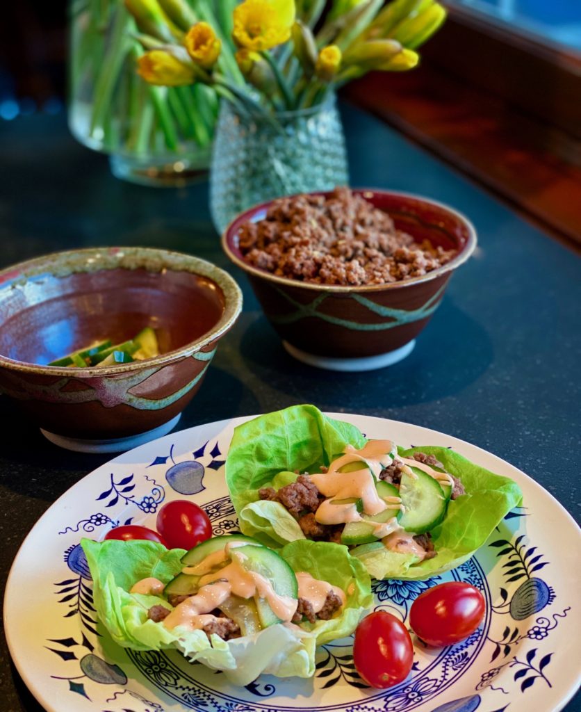 A blue and white plate with cups of lettuce filled with ground beef and a sauce surrounded by small tomatoes 