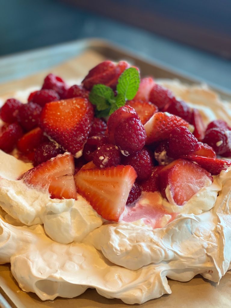 a large pavlova topped with fresh berries on a baking sheet. 