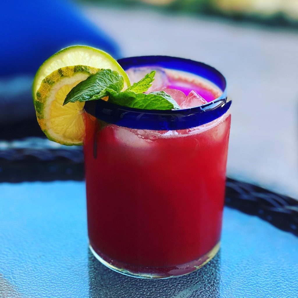 A glass filled with bright red Bacardi rum watermelon agua Fresca garnished with a lime slice and mint