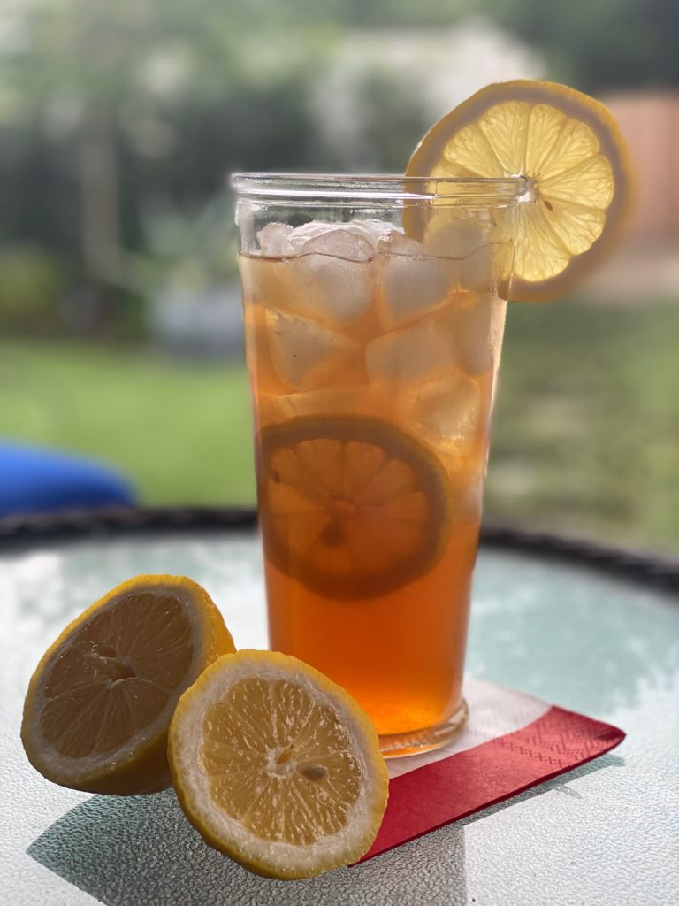 a tall glass of iced tea with a wheel of lemon slice and a sliced open lemon next to the glass 
