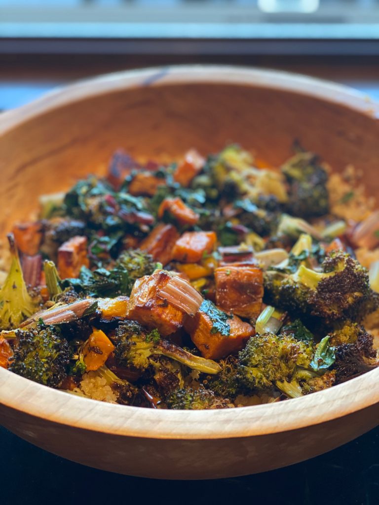 a wooden bowl filled with roasted broccoli and squash 