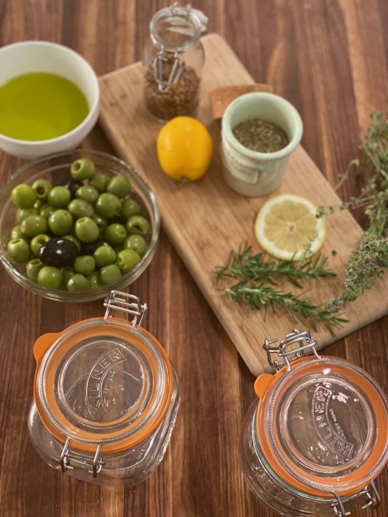 two glass canning jars next to a bowl of green olives and branches of rosemary jar with