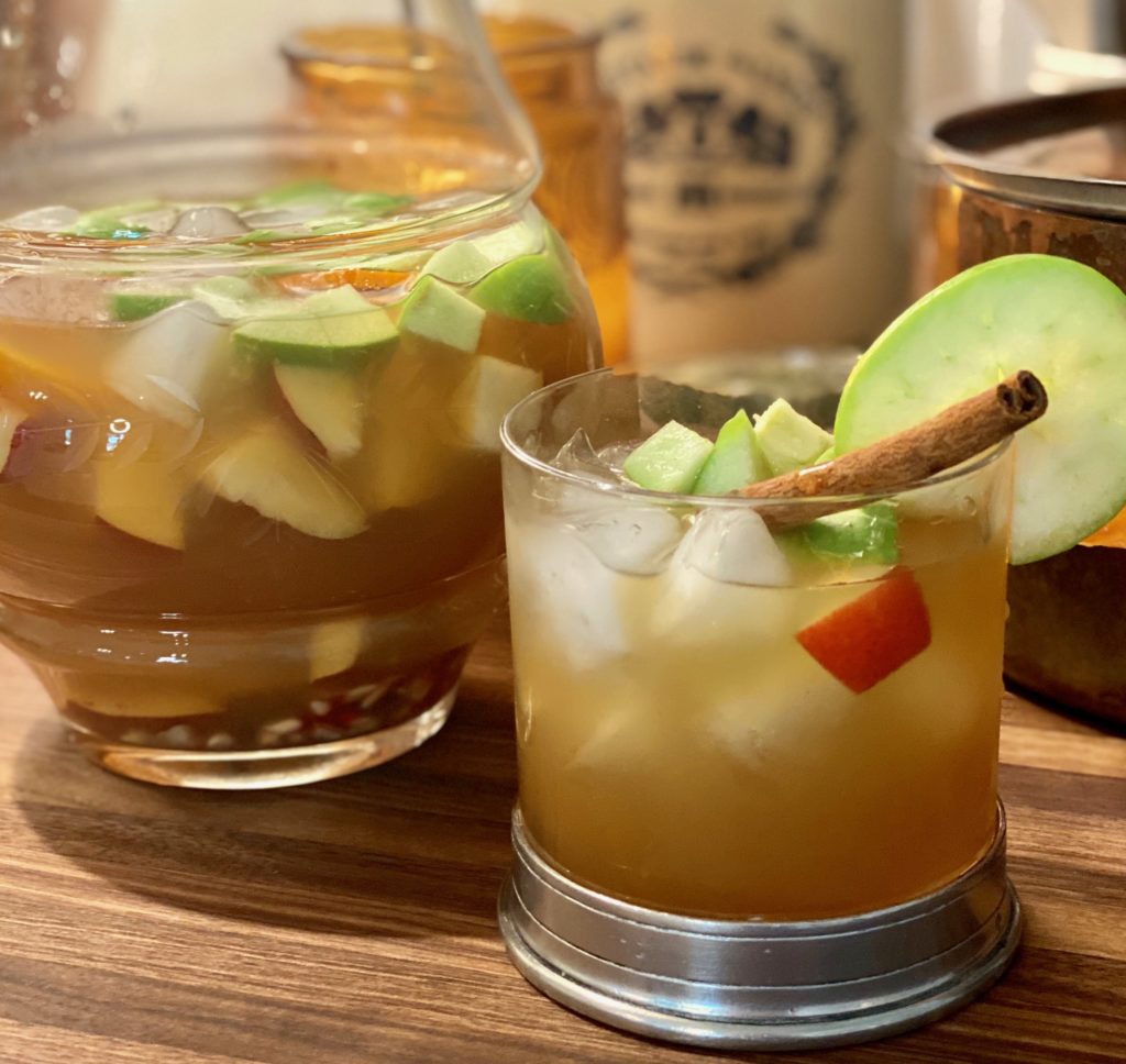 a crystal glass filled with apple cider, a cinnamon stick and chopped apples and pears