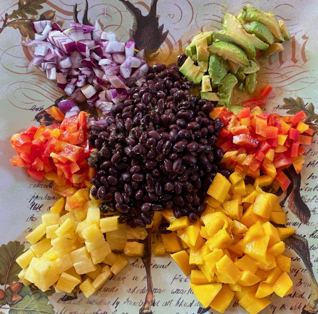 A platter filled with piles of chopped avocado, pineapple, mango, peppers, onions and black beans