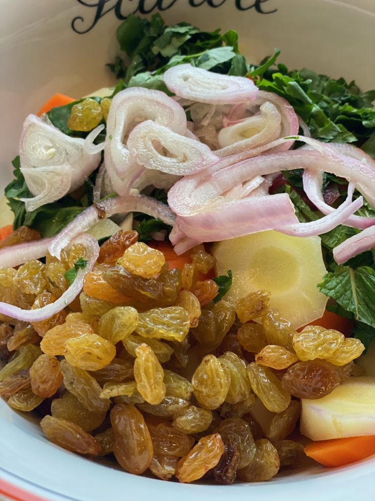 a white ceramic bowl of herbs with carrots , shallots and golden raisins