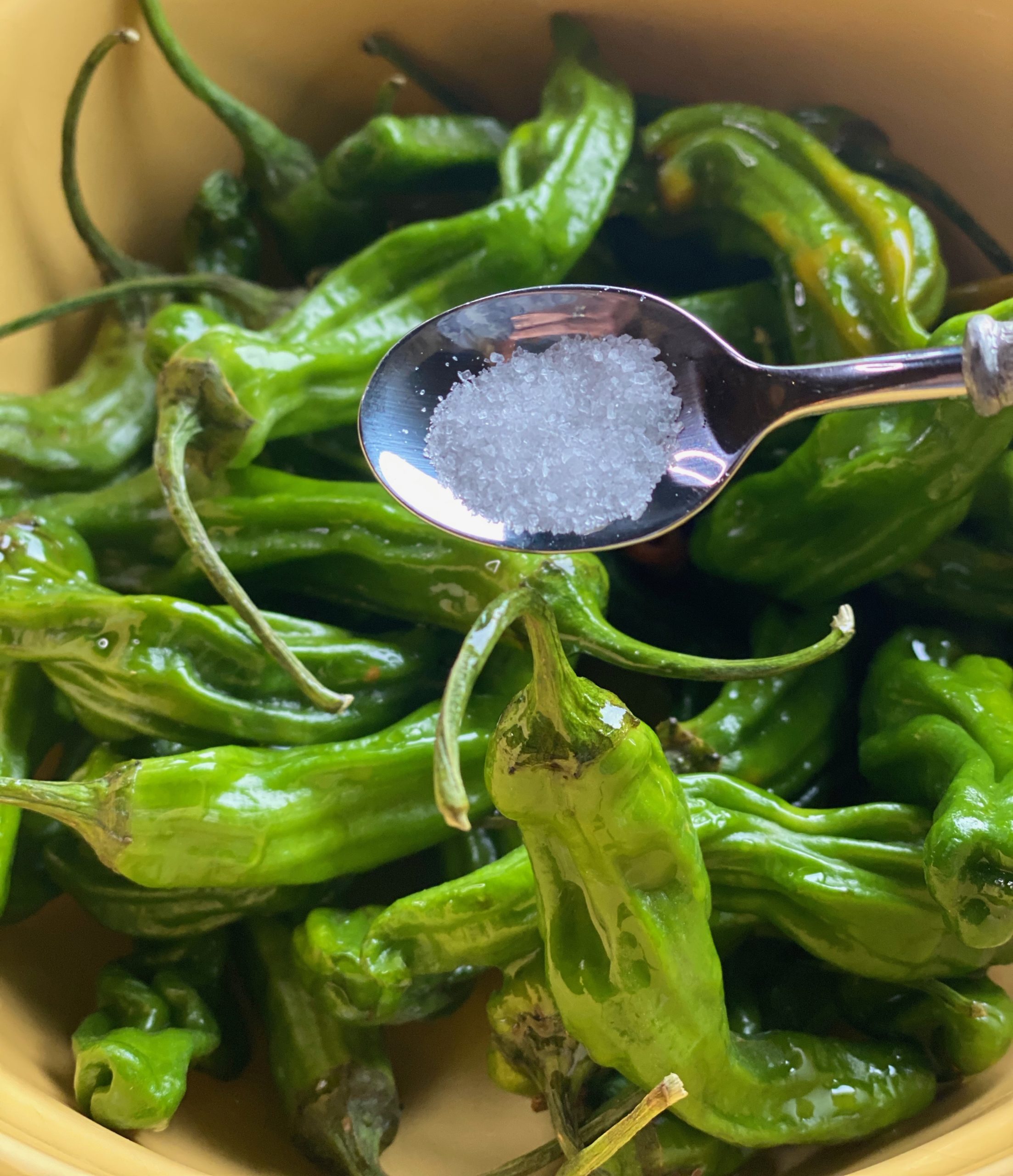 A spoon with salt being poured onto peppers coated in oil