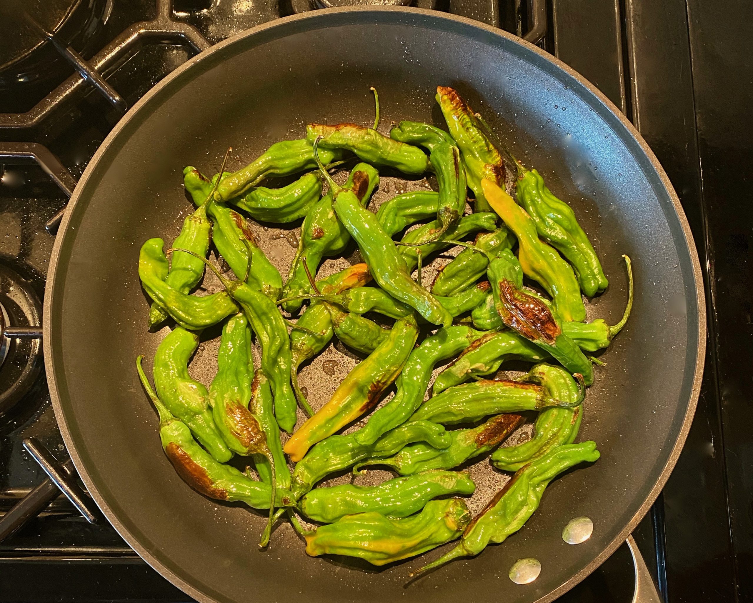 A skillet filled with blistered shishito green peppers