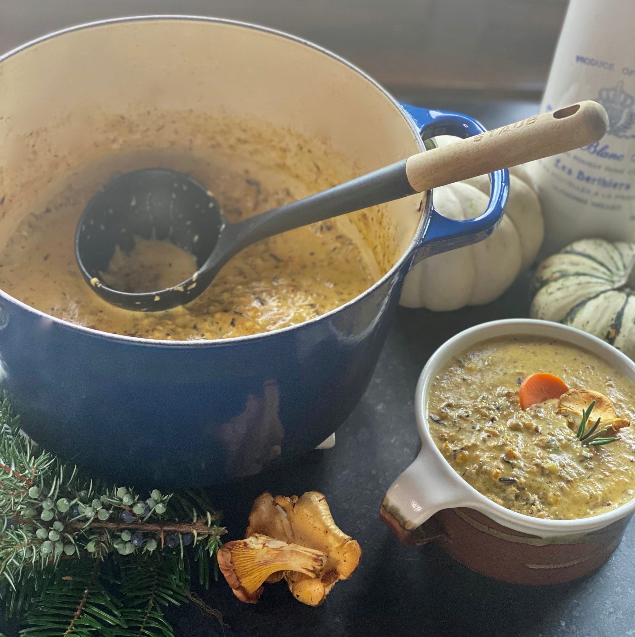 A blue dutch oven with rice and mushroom soup, a ladle with a wooden handle and a bowl of soup with mushrooms scattered around it.