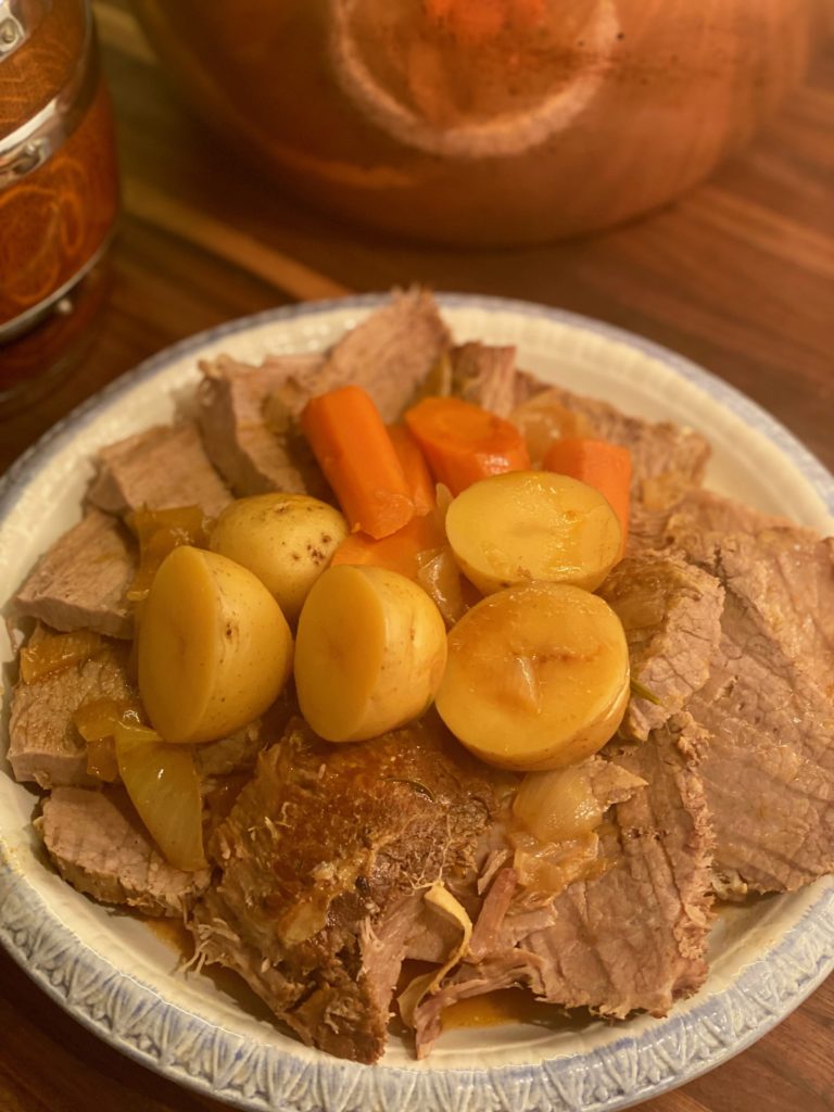 a pile of roast beef surround by carrots and potatoes 