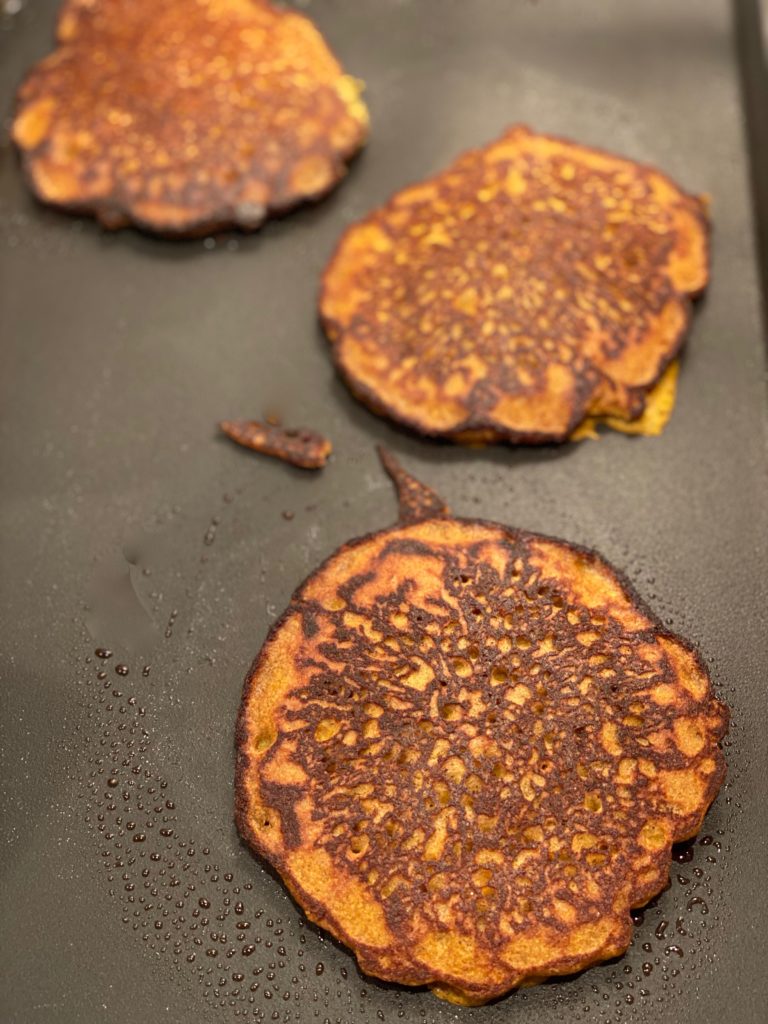 a griddle with dark brown pancakes baking 