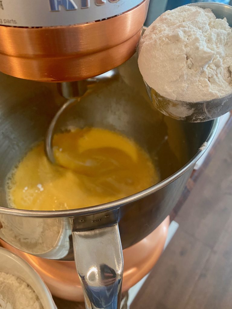 An large mixer with an egg mixture and flour in a measuring cup 