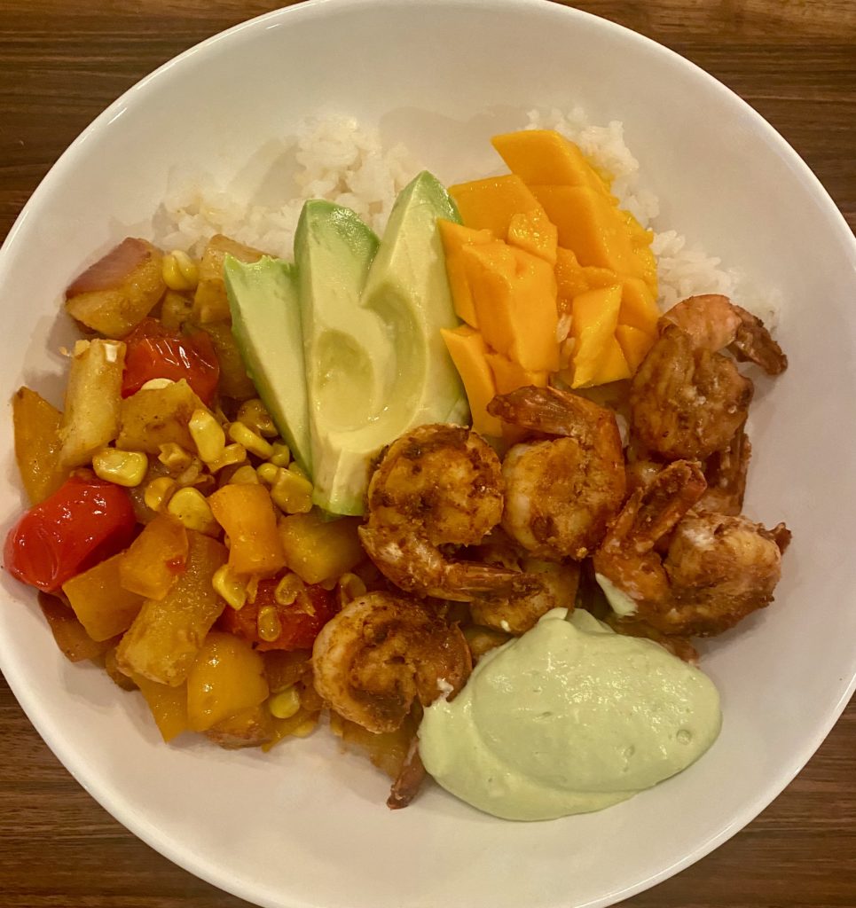 a white bowl filled with spice coated shrimp, pineapple salsa and sliced avocados
