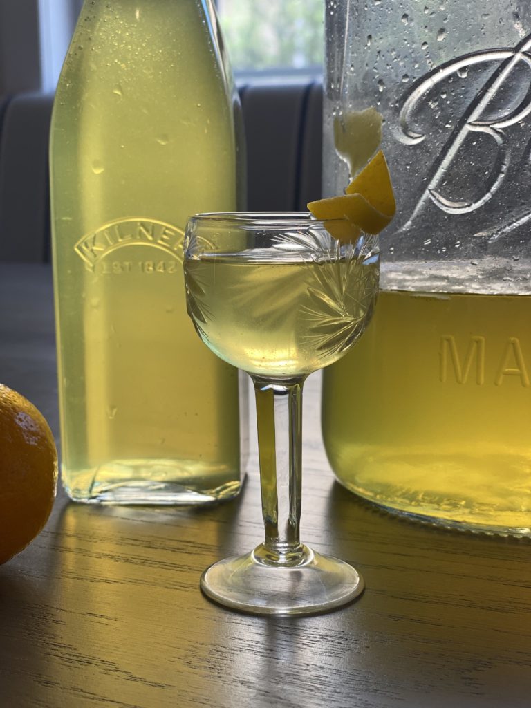 A sherry crystal glass  filed with yellow liquid and rimmed with lemon peel 