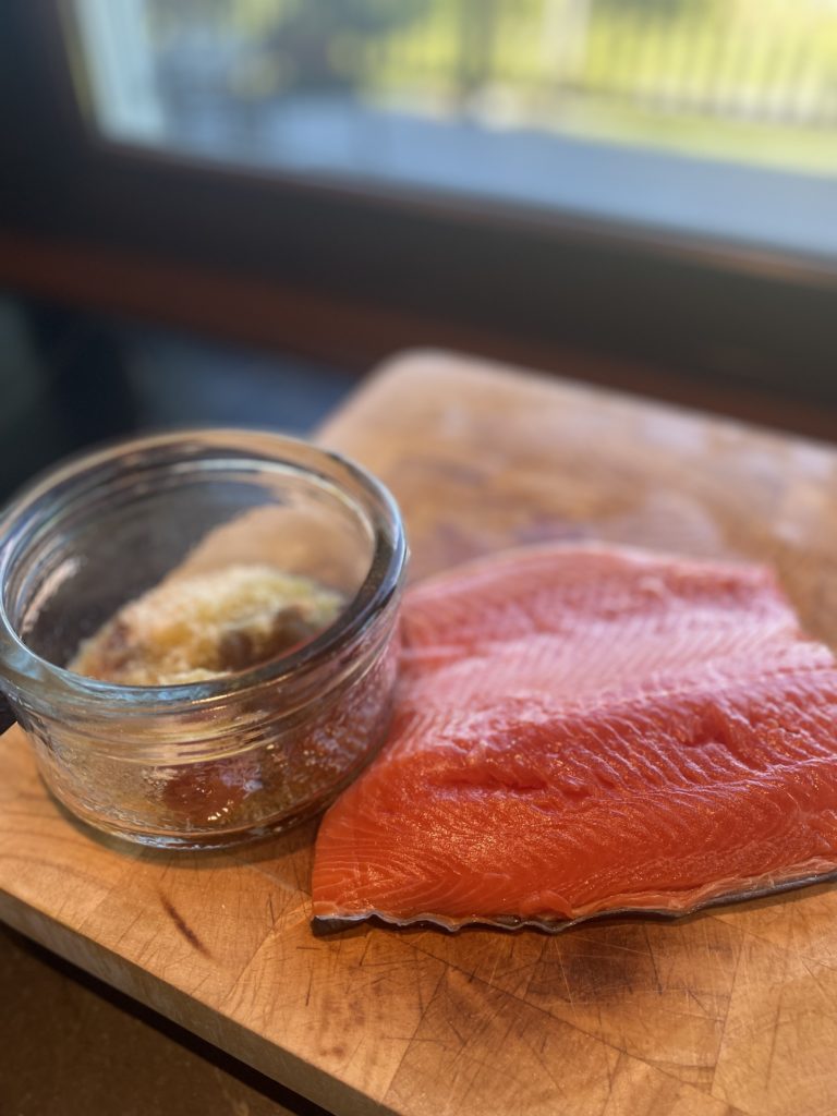a large piece of uncooked salmon on a wooden board next to a bowl of spices 