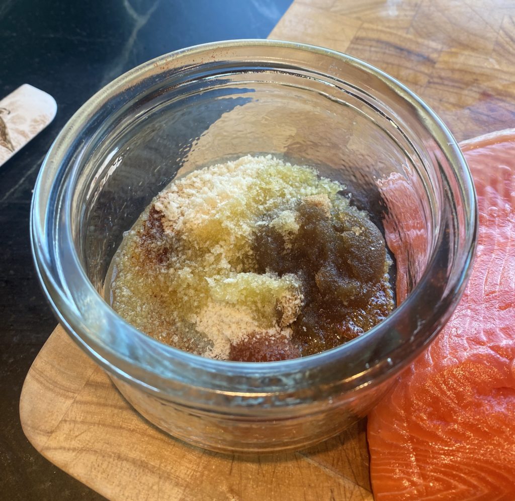 a glass bowl filled with spices next to a piece of salmon 
