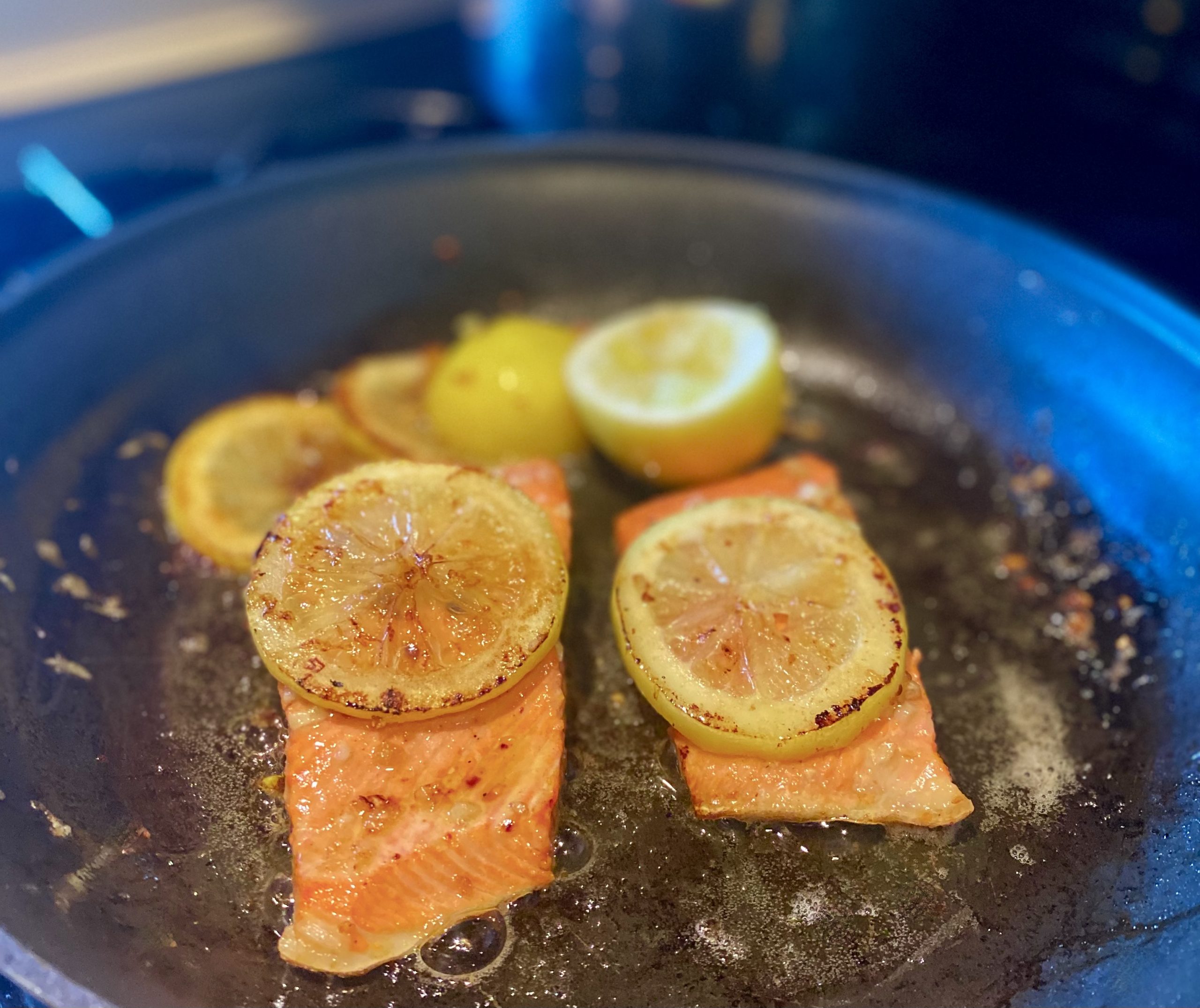 two salmon filets cooking in a pan filled with lemons