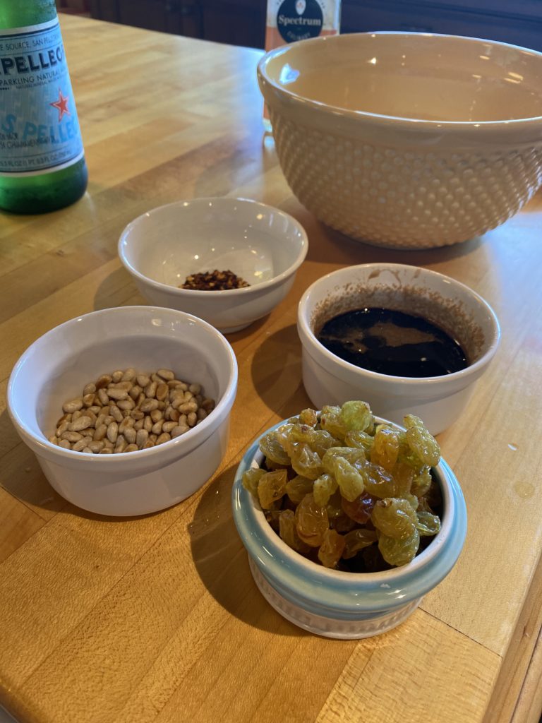 small bowls filled with raisins, pine nuts, red pepper flakes and vinegar 

