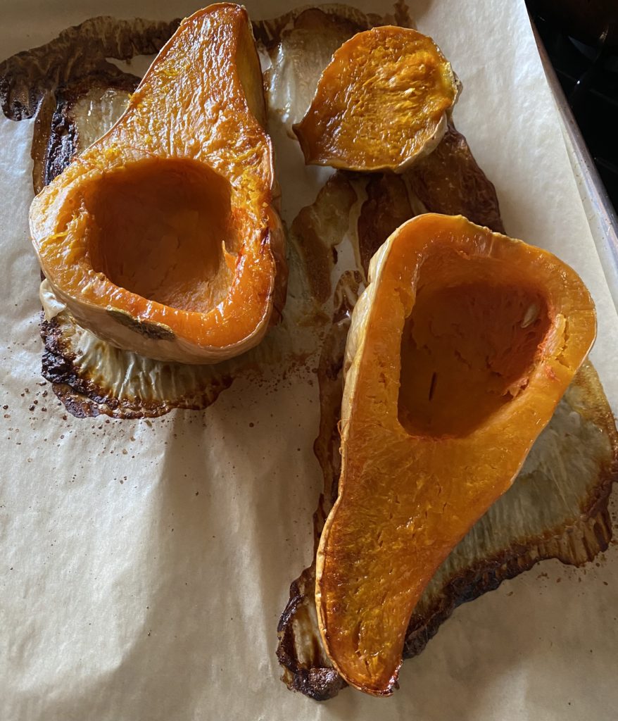 A butternut squash that has been roasted sliced in half on a sheet pan that is covered with parchment paper