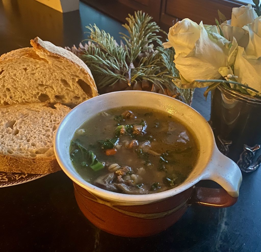 A bowl of soup, bread on a plate a white roses 