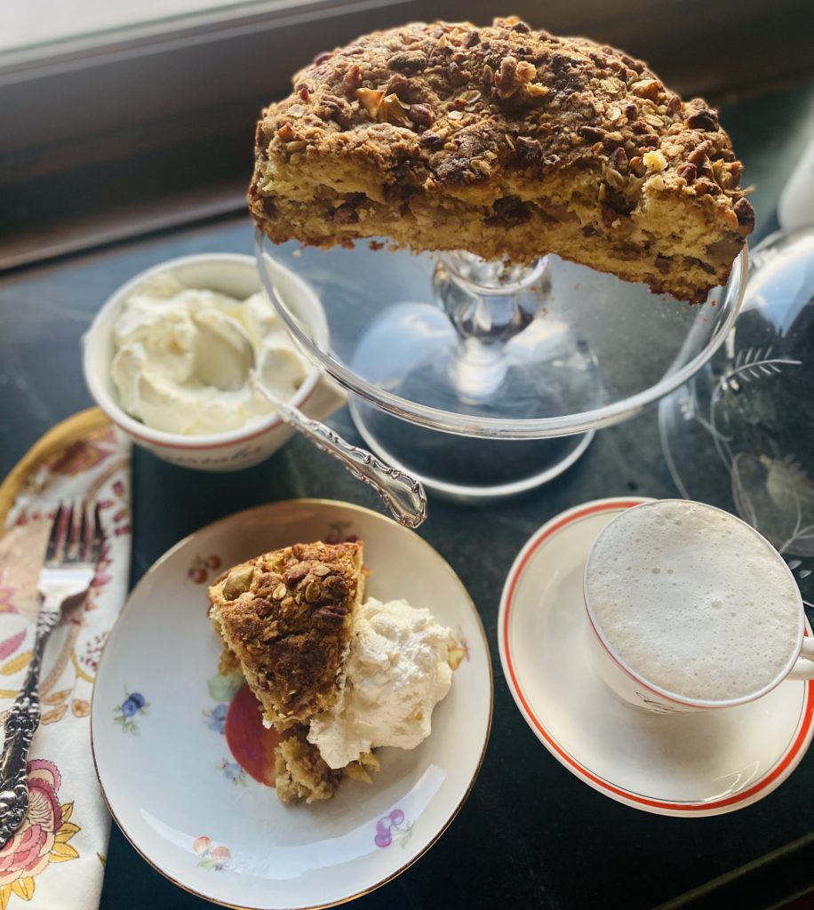 a glass cake stand with a coffee cake and a cup of coffee