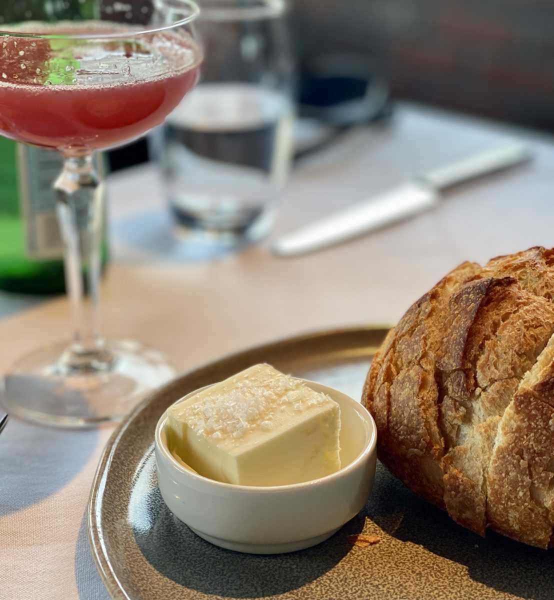 A chuck of butter next to a loaf of sourdough bread and a cocktail 