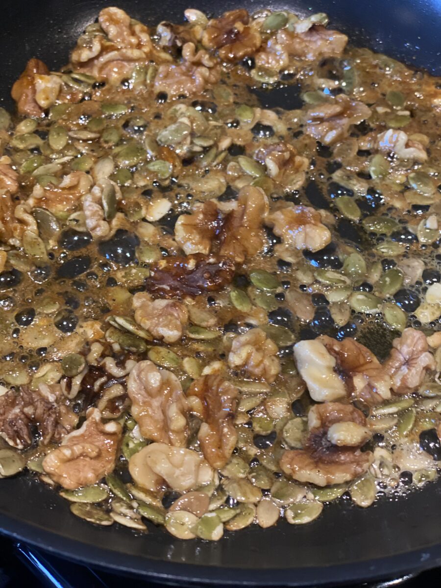a pan with pumpkins seeds and walnut being sautéed in butter and honey 