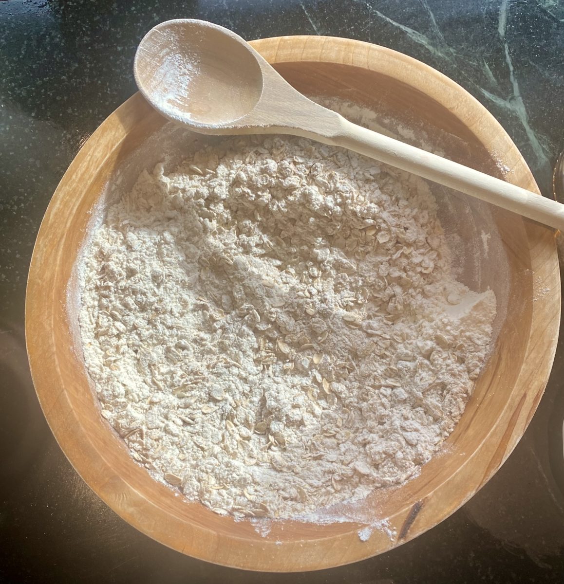 a wooden bowl and spoon filled with flour mixed with dry oatmeal