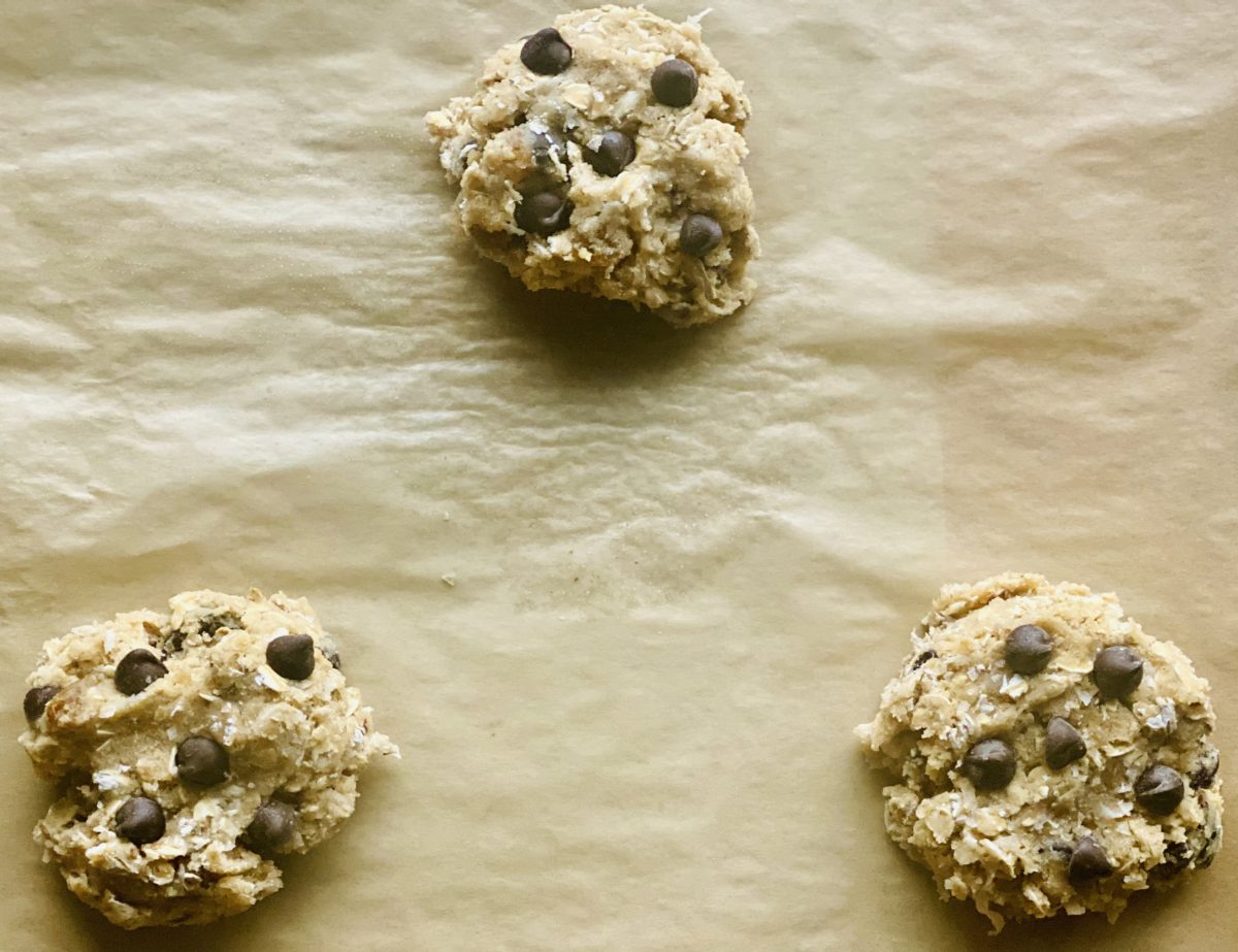 three cookies dotted with chocolate chips resit on parchment paper ready for the oven