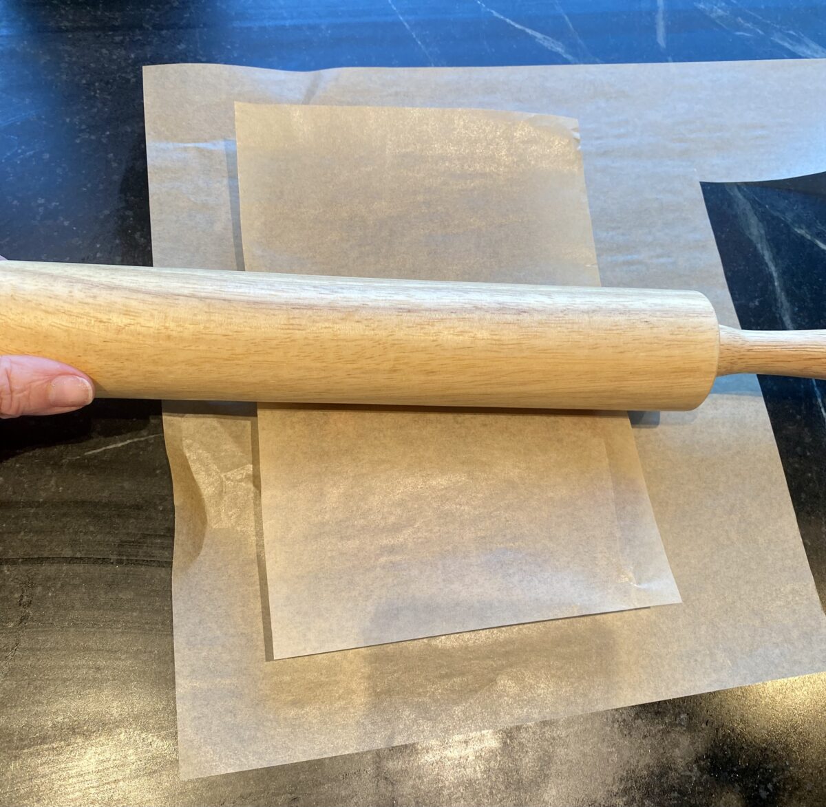 a rolling pin pressing the dates flat in between two sheets of parchment paper 