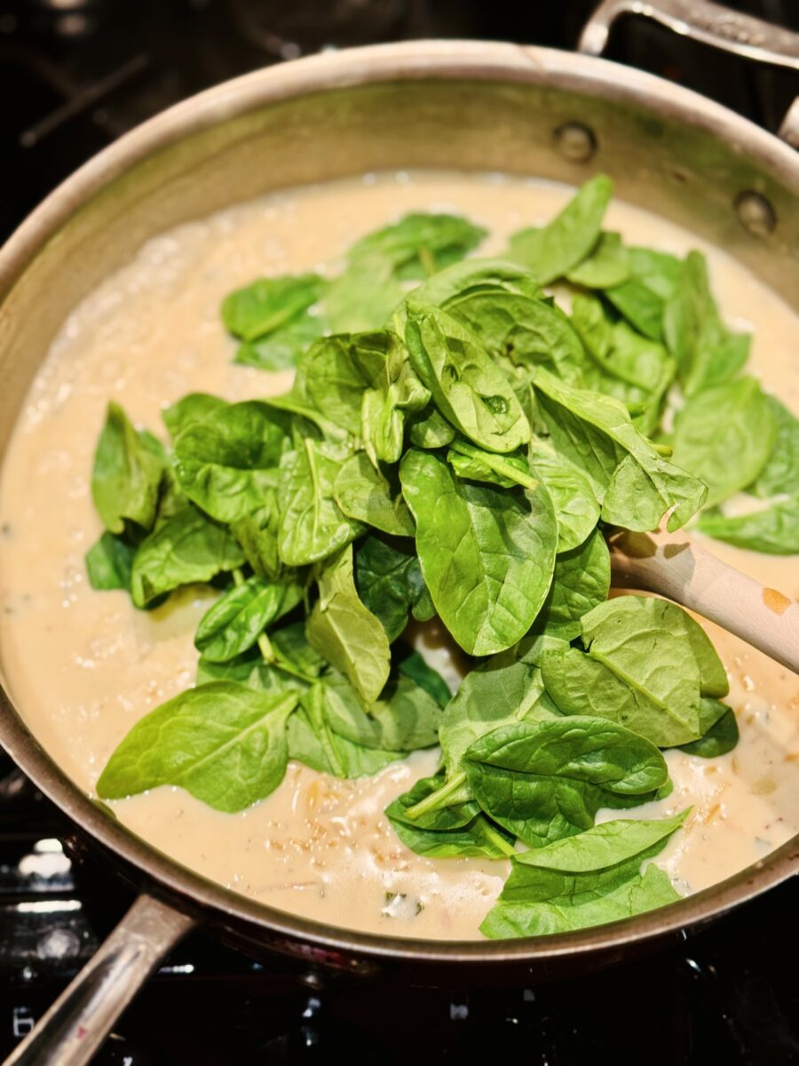 a pan of cream sauce and fresh spinach in a pan 