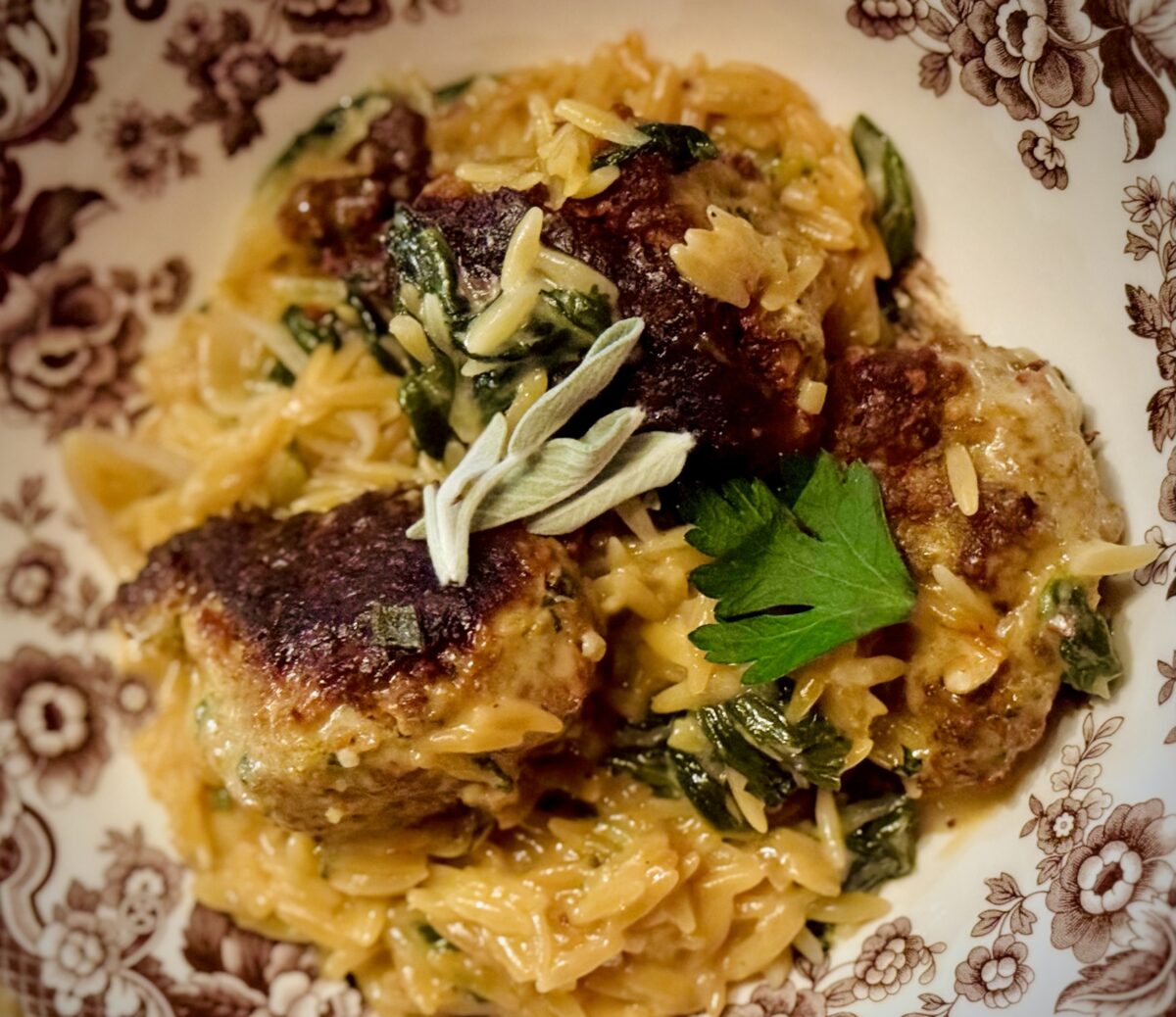 A bowl filled with creamy orzo surrounded with several meatballs 