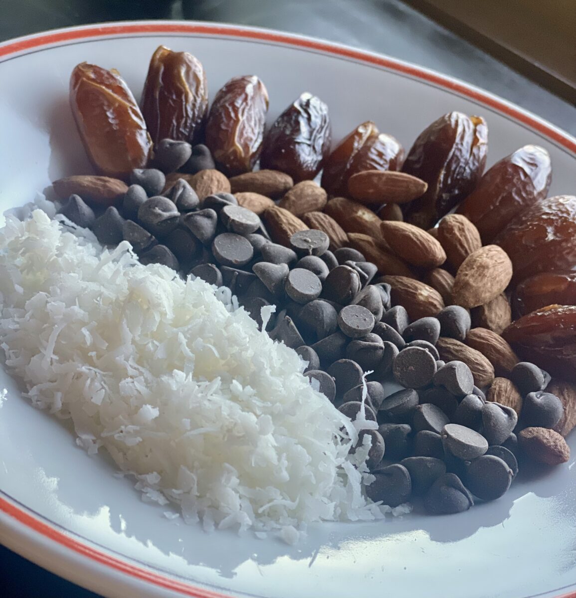 coconut, dark chocolate chips, almonds and dates on a white plate 