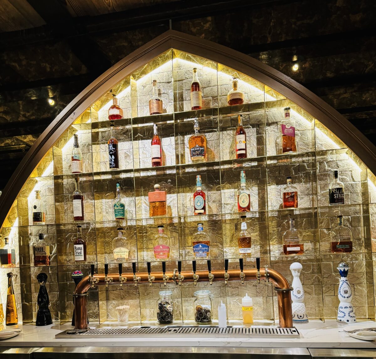 a bar with an arched set of shelves filled with spits lit up from behind 