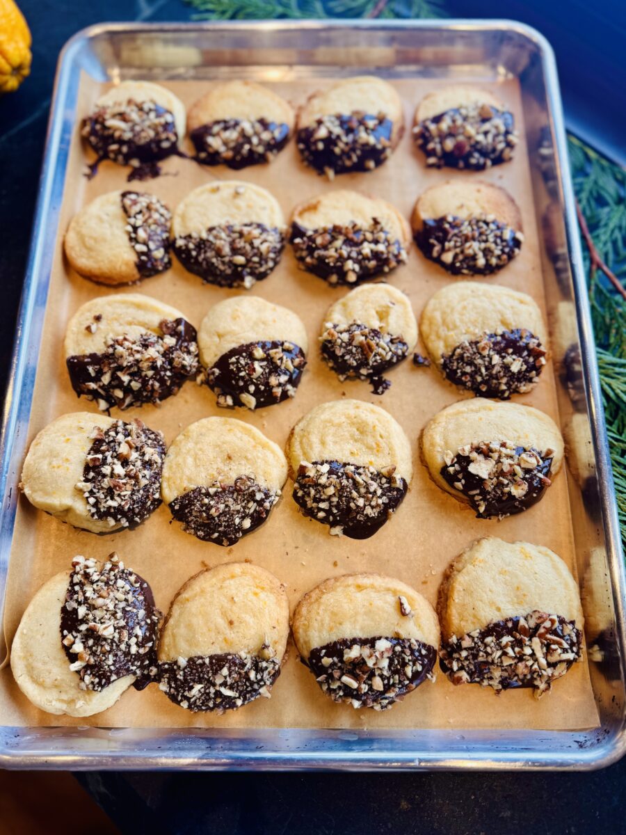 Tray pf prange shortbread dipped in dark chocolate and topped with finely chopped pecans on a parchment lined rimmed baking sheet