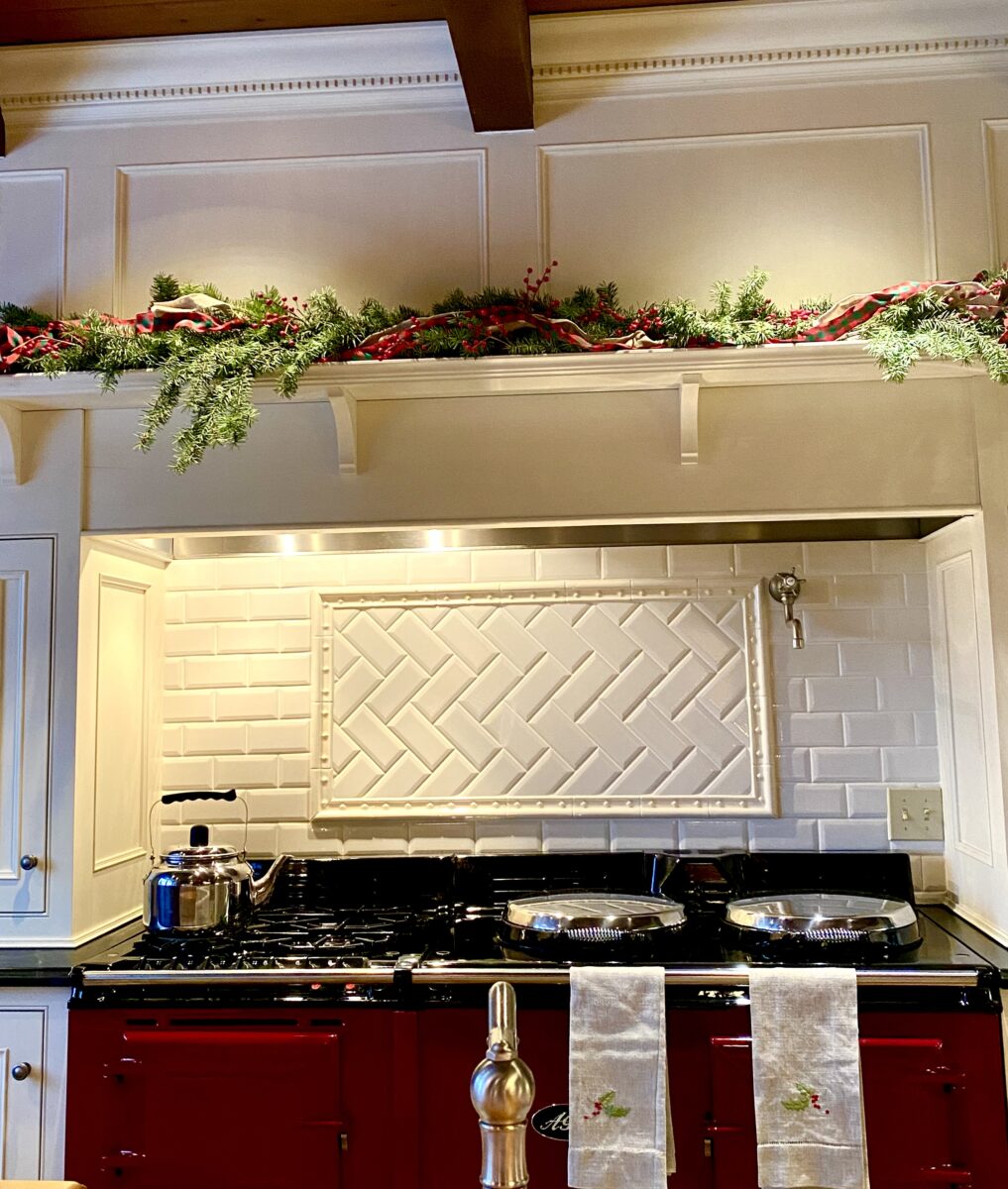 a red AGA range with a mantle above it decorated with swags of cedar branches 
