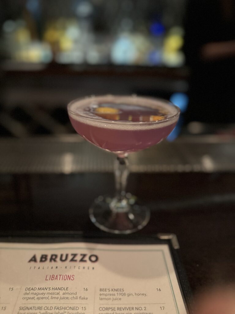 a pink cocktail in a coupe glass with a lemon garnish
