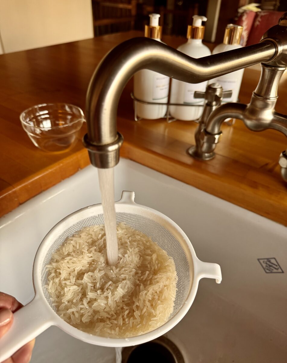 a white sieve filled with rice being rinsed over a sink 