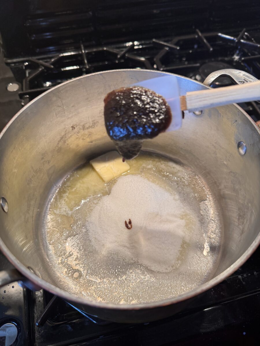 a heaping tablespoon of vanilla bean paste being spooned into a saucepan of melted butter 