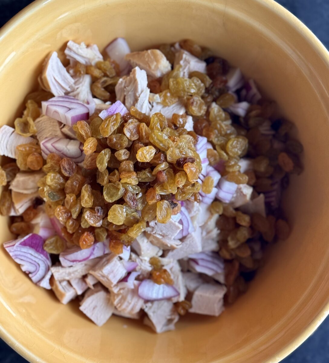 chopped chicken, purple onions and golden raisins in a yellow ceramic bowl 