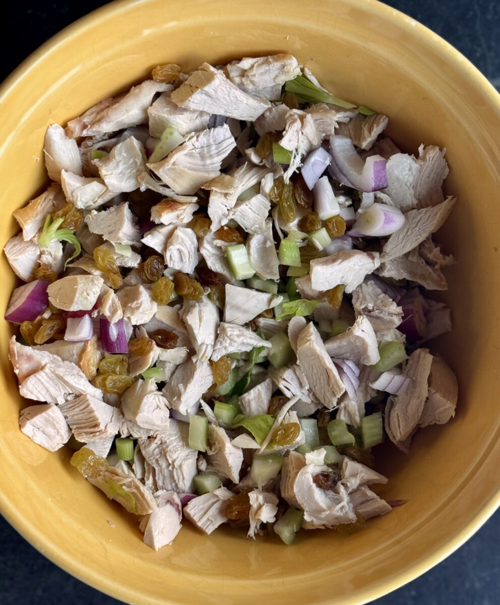 chopped chicken breasts, celery, purple onions and golden raisins  in a yellow ceramic bowl. 