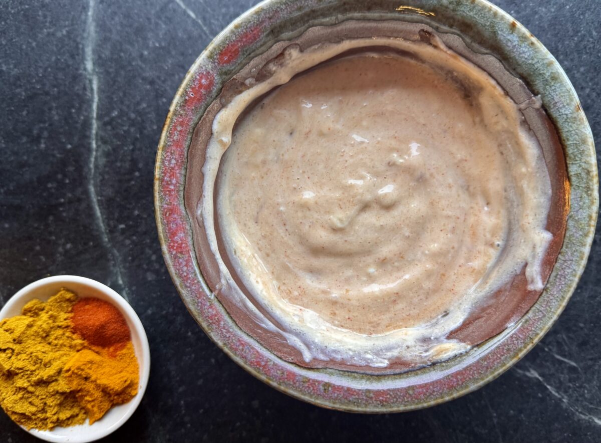an earthenware bowl of greek yogurt and mayonnaise and a bowl of curry spices 