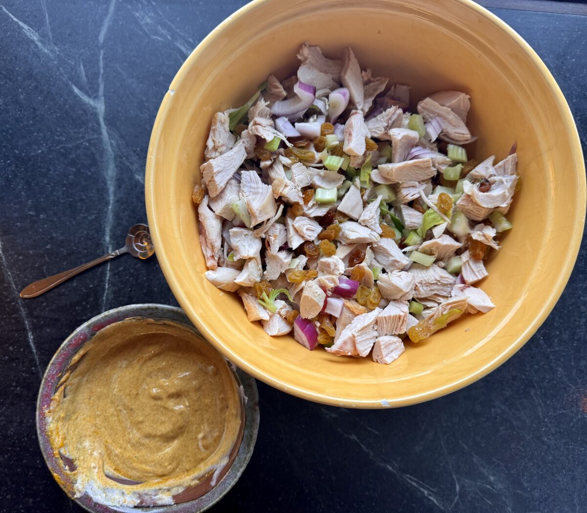 a bowl of chopped chicken and vegetables next to an earthenware bowl of curried mayonnaise  about to be  tossed into a curry chicken salad 