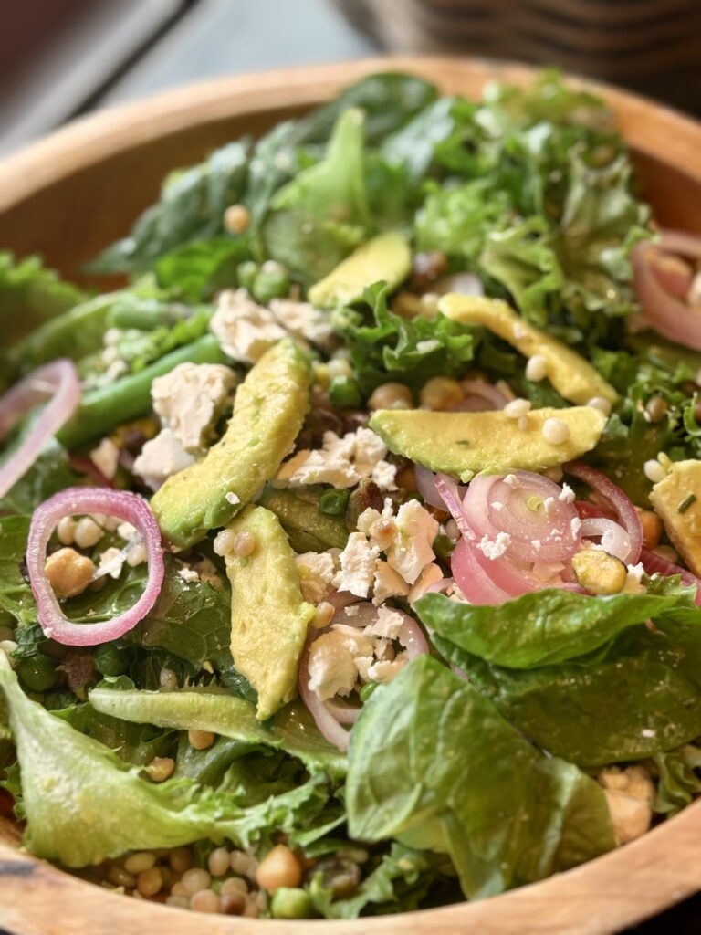 a wooden bowl filled with spinach , chickpeas, feta, shallots and avocado
