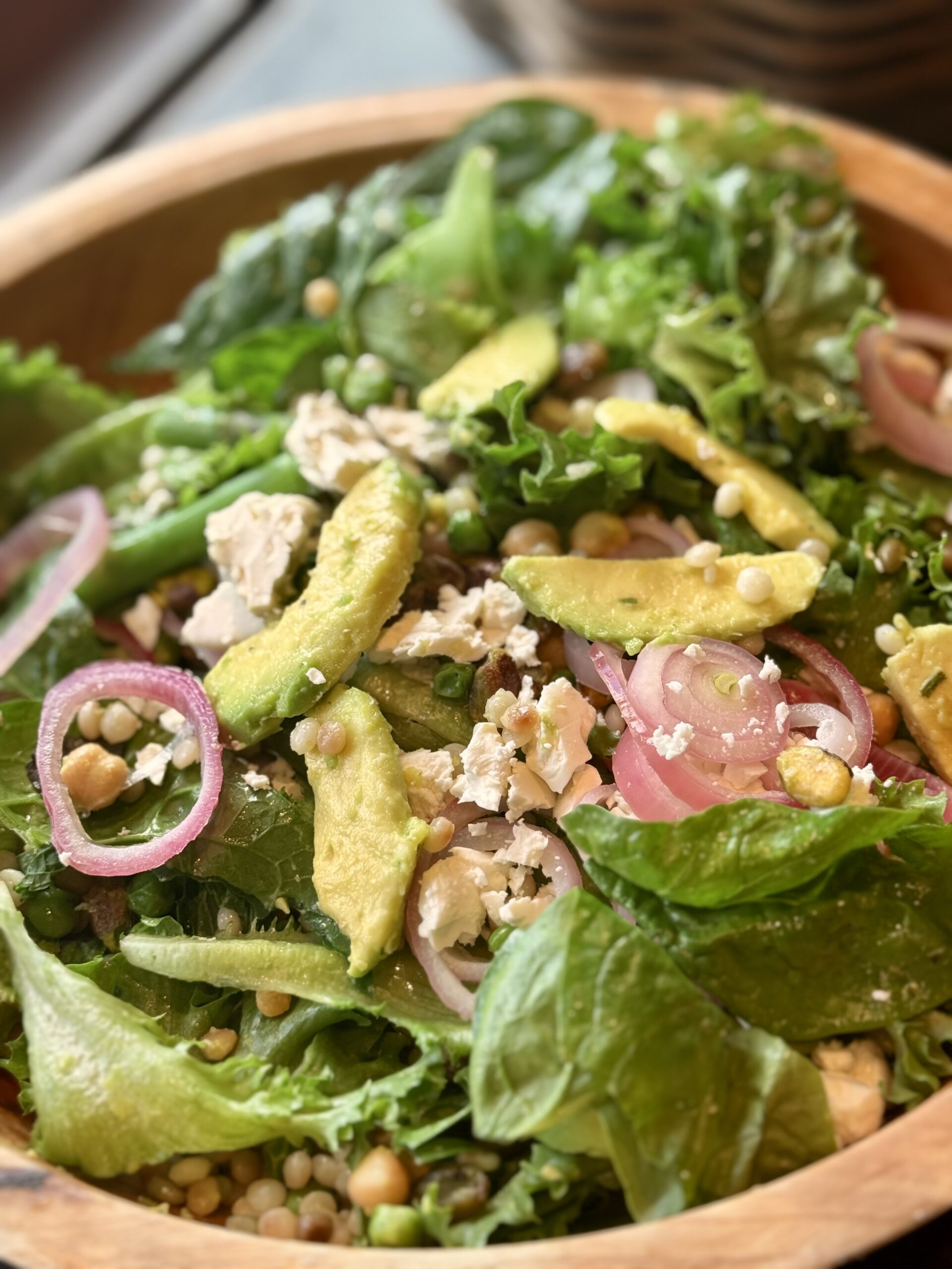 a wooden bowl filled with spinach , chickpeas, feta, shallots and avocado