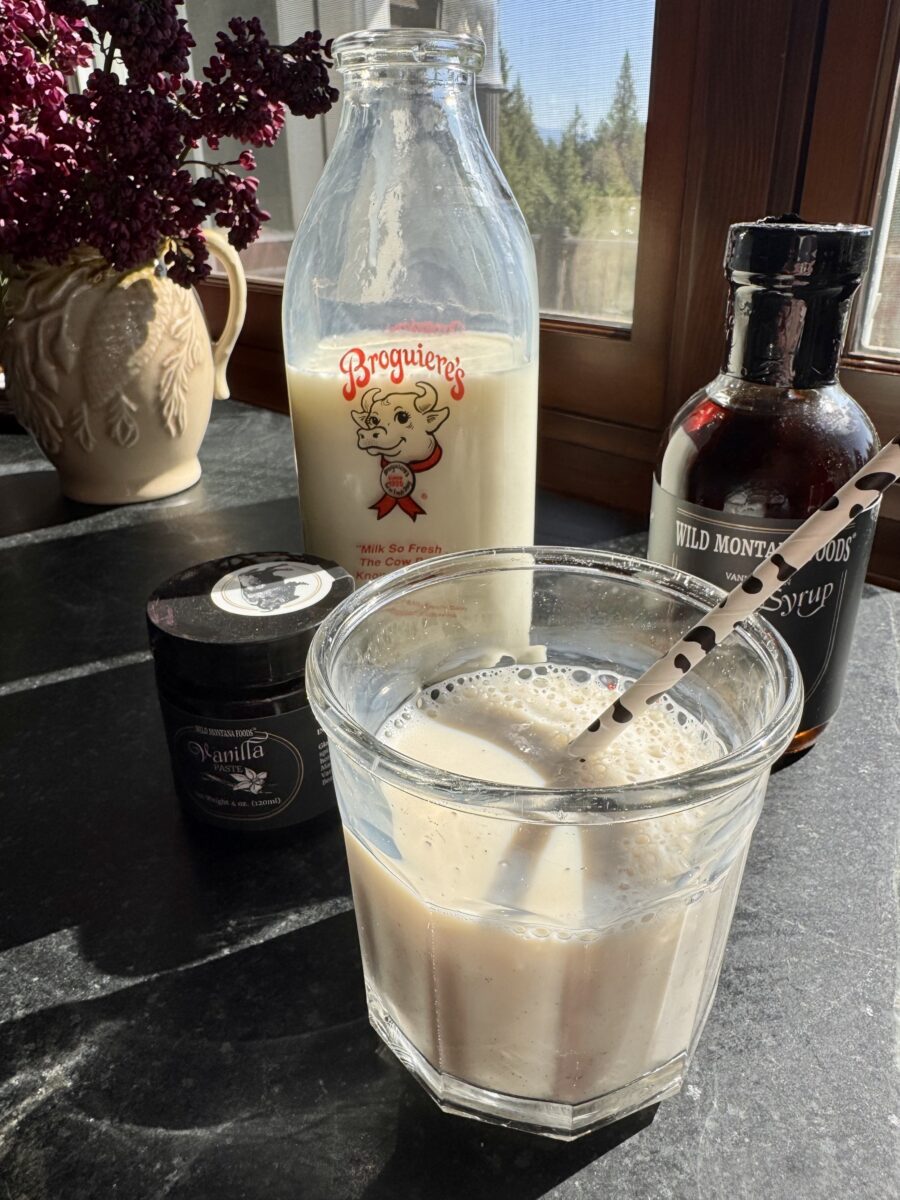 a glass filled with vanilla milk next to a jar of vanilla bean paste