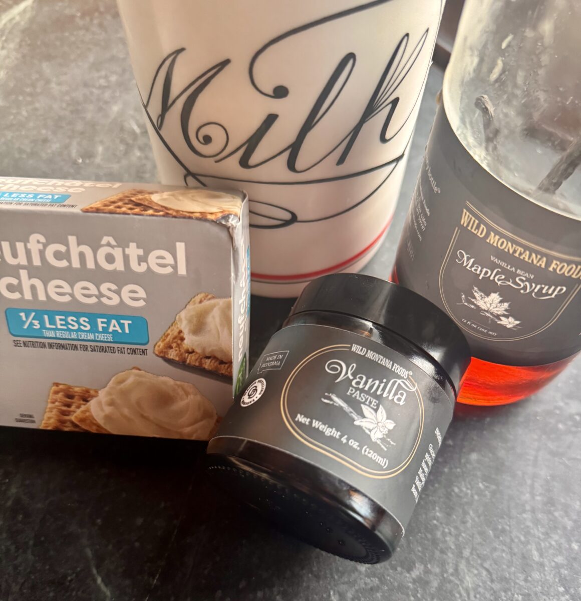 a white and red milk bottle next to a bottle of wild Montana Foods vanilla bean paste and maple syrup and a box of cream cheese 