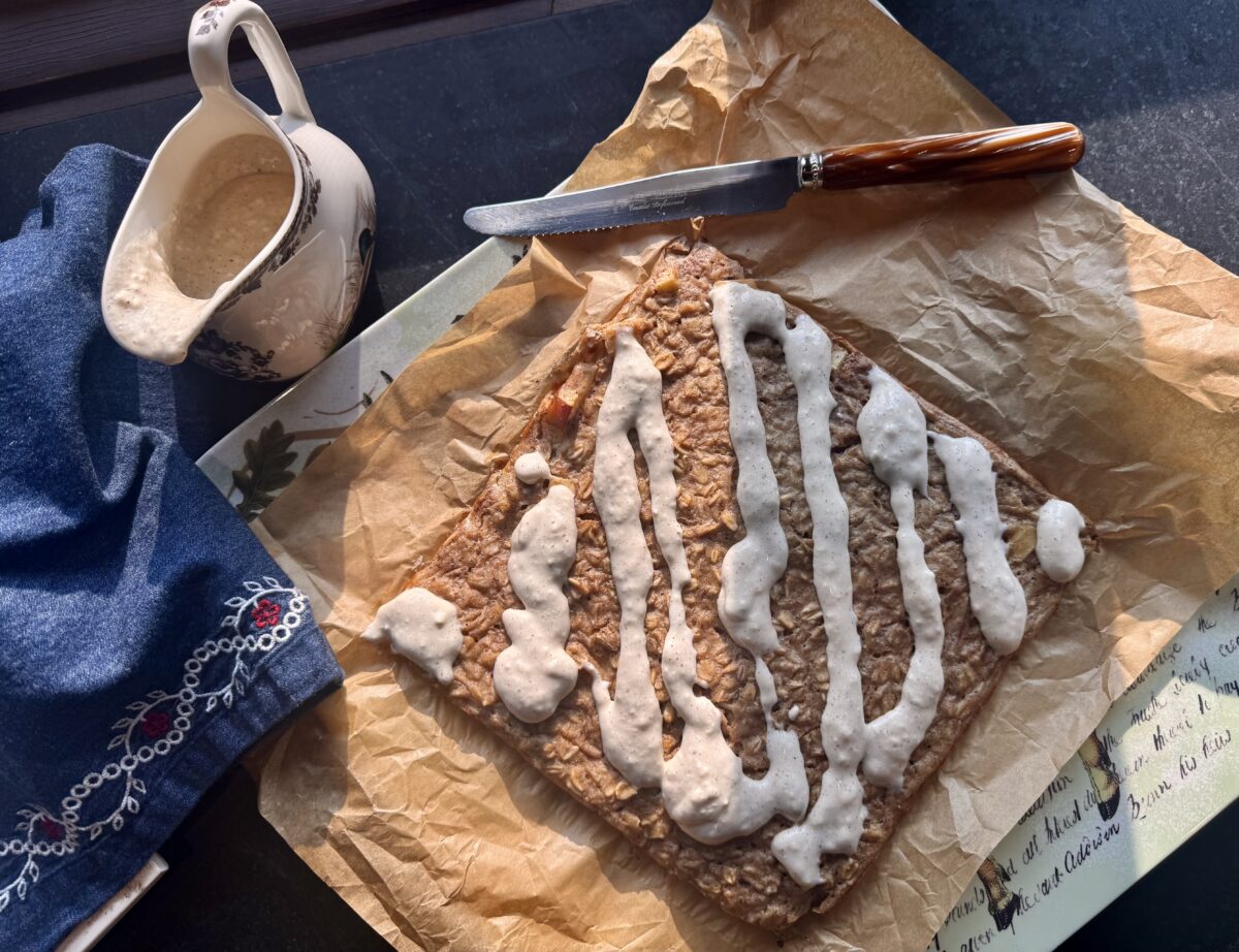 A square of baked overnight oats drizzled with a glaze next to a small pitcher of icing